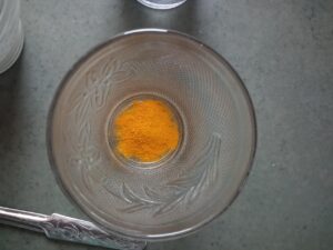 Donna che versa acqua in un bicchiere con curcuma, preparandosi a bere per sgonfiare la pancia.